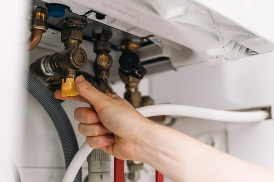 Main tenant ajuste une vanne d'arrêt rouge sur canalisation de chauffage murale