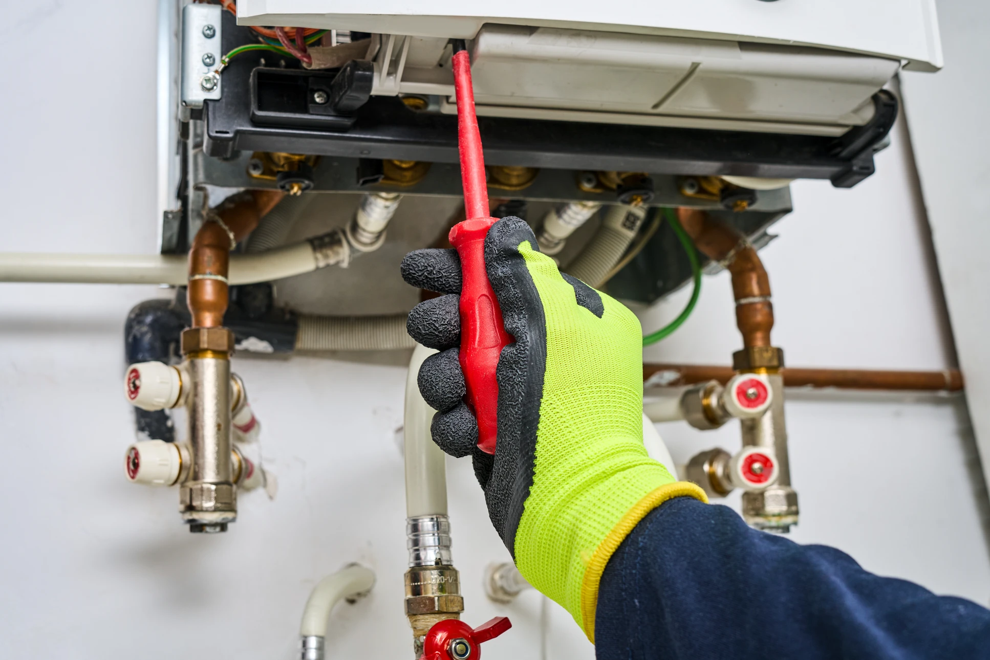 Technicien en tenue professionnelle (combinaison ou polo de travail) effectuant une intervention de maintenance ou dépannage sur une chaudière fioul ou ses équipements périphériques, dans un intérieur de maison ou petit bâtiment professionnel. Le technicien est concentré et utilise ses outils ou effectue une inspection/diagnostic. La scène doit transmettre la professionnalité, la réactivité et la compétence technique du service d'entretien et dépannage.